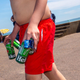 Man in swim trunks carries empty beer cans